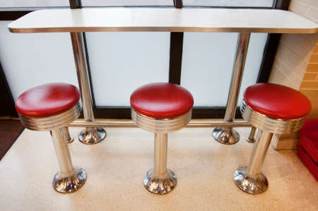 Three vintage red seat diner stools facing counter and window.