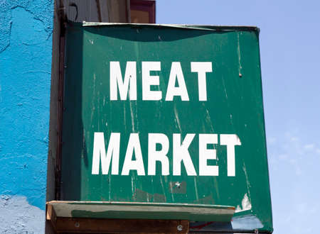 Weathered white lettering on MEAT MARKET sign streaked with bird droppings attached to building.の写真素材