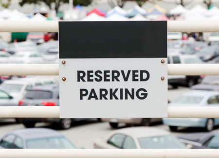 RESERVED PARKING sign on metal railing with parked cars in defocused background. Copy space on area...