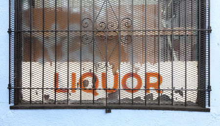 Shabby LIQUOR store sign behind rusty window security grate.