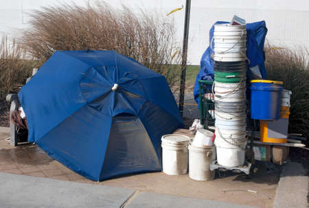 Homeless person`s belongings and buckets for can collection protected with umbrella.の写真素材