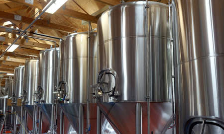 Row of shiny metal micro brewery tanks.