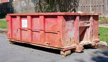 Red industrial dumpster on neighborhood street.の写真素材