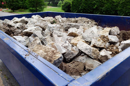 Dumpster filled with sidewalk concrete debris in neighborhood setting.の写真素材