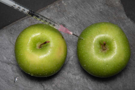 A green apple being injected with a syringe containing red fluid, isolated on bkuck background....