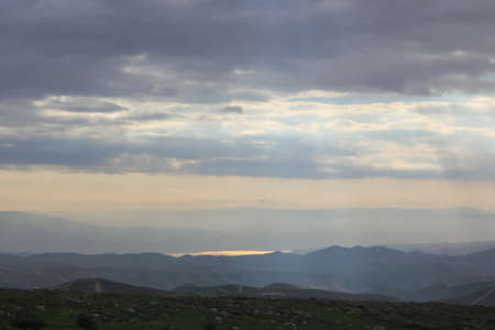Beautiful sunrise of Judean Desert wadi, with sun rays breaking through clouds over the dry riverbed of Nahal Dragot popular hiking trail, winding towards the Dead Sea Israelの写真素材