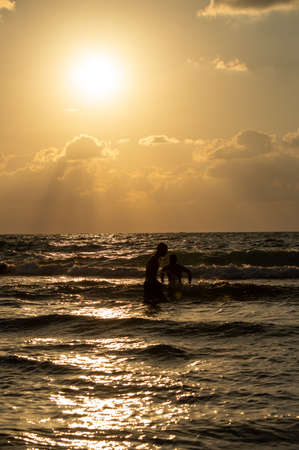 People are playing in the sea against a red sunset with clouds . Gold seaの写真素材
