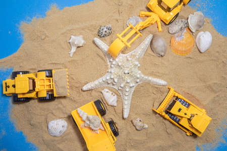 Orange plastic toy tractor with bucket build shells tower of sand. Space for text..の写真素材