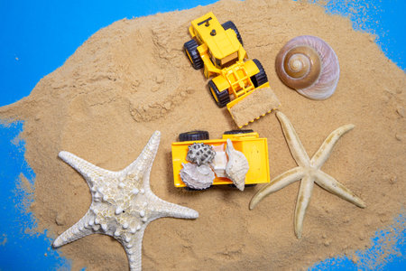 Orange plastic toy tractor with bucket build shells tower of sand. Space for text.. High quality...