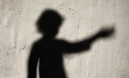 A blurred shadow silhouette of a child reaching out with an extended arm against a textured wall, symbolizing asking for help, vulnerability, and support.の素材