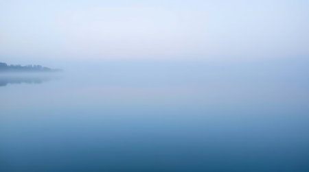Experience the profound peace of a misty lake at dawn. Distant trees fade into the soft haze, reflecting a tranquil, serene atmosphere perfect for calm contemplation or natural beauty projects.の素材