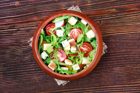 Fresh salad with rucola, tomato, cheese and toast bread on an old brown wooden table, top view(selective focus).の写真素材