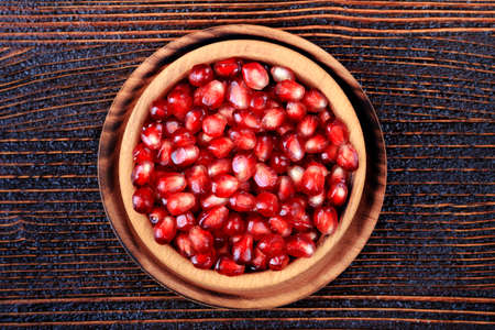 Fresh pomegranate seeds in bowl on an old brown wooden table, top view(selective focus).の写真素材