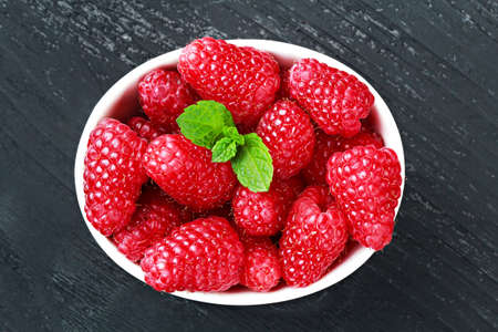 Fresh raspberries in a white bowl on old black wooden background, top view(selective focus).の写真素材