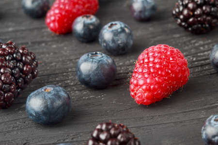 Fresh blueberries, raspberries and blackberries on old  black wooden background, selective focus.の写真素材