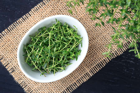 Fresh savory leaves in a white bowl on old black wooden background, top view (selective focus).の写真素材