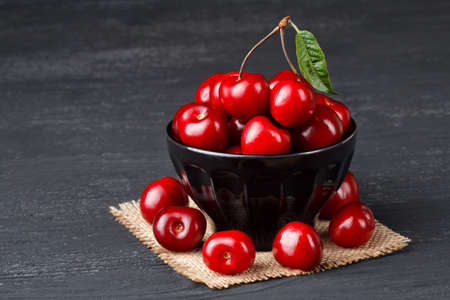 Fresh cherries in bowl on old black wooden table(selective focus).の写真素材