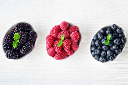 Fresh blueberries, raspberries and blackberries in bowl on old white wooden background, top view(selective focus).の写真素材