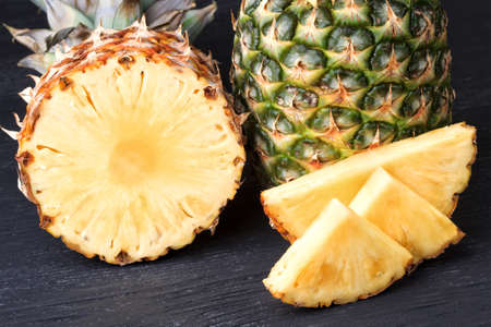 Fresh pineapple tropical fruit (ananas) sliced and whole.Summer fruit on a black wooden table (selective focus).の写真素材
