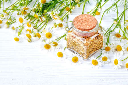Dried and fresh chamomile flowers and leaves in bottle. Alternative medicine concept on a white wooden table(selective focus).の写真素材