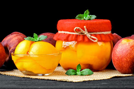 Preserved peach compote with half peaches in glass jars on an old black wooden table(selective focus).の写真素材