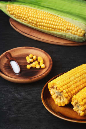 Cooked and raw corn on black wooden table (selective focus).の写真素材