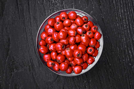 Hawthorn berries (crataegus) in glass bowl on a old black wooden table, top view (selective focus).の写真素材