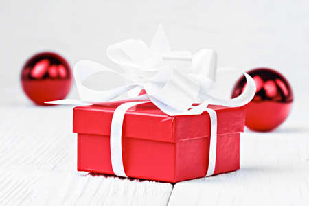 Red Christmas gift box with white bow on white wooden table (selective focus).の写真素材