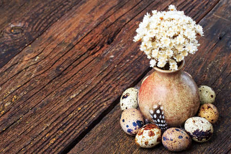 Quail eggs and dried flowers in little vase on old wooden table, top view. Easter vintage style  (selective focus).の写真素材