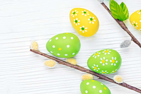 Colorful Easter eggs and willow branches on white wooden background, top view