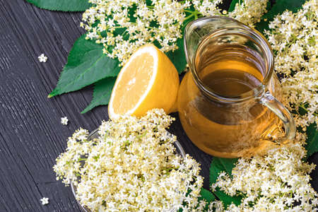 Homemade elderflower syrup in a glass pitcher on black wooden table, top view (selective focus)の写真素材