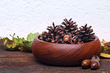 Autumn still life - acorns and pine cones in wooden bowl on an old wooden background (selective...