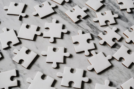 A close-up of white puzzle pieces scattered over a textured marble surface, ideal for representing creativity, problem-solving, and playful learning.の素材