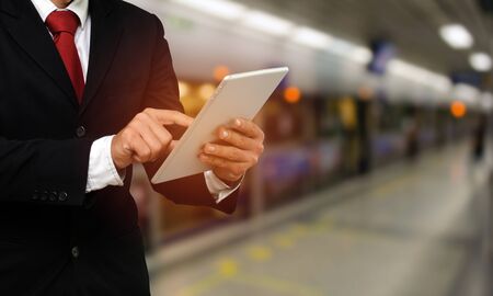 smart businessman in suit using his tablet, business and technology concept with blurred subway station background.の写真素材