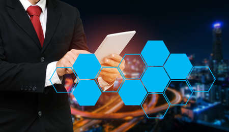 smart businessman in suit using his tablet, business and technology concept with blank hexagonal shaped pattern and blurred night city background, copy space.の写真素材