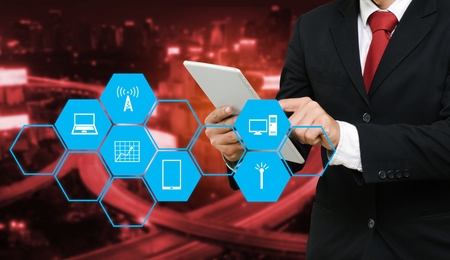 smart businessman in suit using his tablet, business and technology concept with technology device icon in hexagonal shaped pattern and blurred night city background, copy space.の写真素材