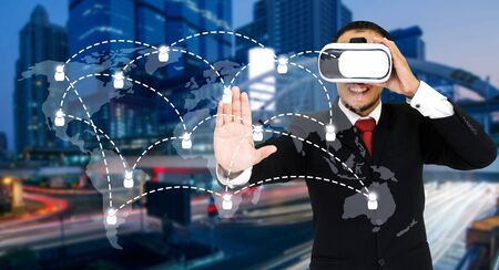 Young asian businessman wearing VR virtual reality headset, business and technology concept for future with world map social media connection on blurred night cityの写真素材