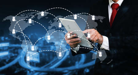 smart businessman in suit using his tablet, business and technology concept with world map social media network connection on blurred night city background, color tone effect.の写真素材