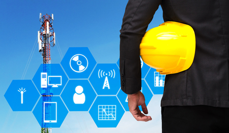 businessman with yellow safety helmet with technology device icon and hexagon shaped pattern background with telecommunication tower with blue sky,  technology business industrial concept,の写真素材