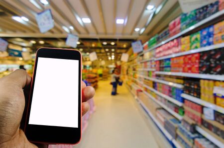 hand holding smart phone blank screen for advertisement with abstract blurred background in supermarket, shopping concept, soft focus, selective focus, copy space, color tone effect.の写真素材