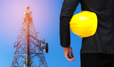 businessman in suite with yellow safety helmet with telecommunication tower with blue sky background, business industrial concept, sunlight effect.の写真素材