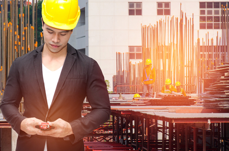 smart construction manager in suite with walkie-talkie or two way radio in hand and yellow safety helmet with construction site workers background, industrial technology and business concept.の写真素材