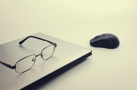 Laptop computer with wireless black mouse and eyeglasses, vintage color tone effect, selective focus, copy spaceの写真素材
