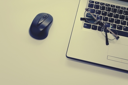 Laptop computer with wireless black mouse and eyeglasses, vintage color tone effect, selective focus, copy spaceの写真素材