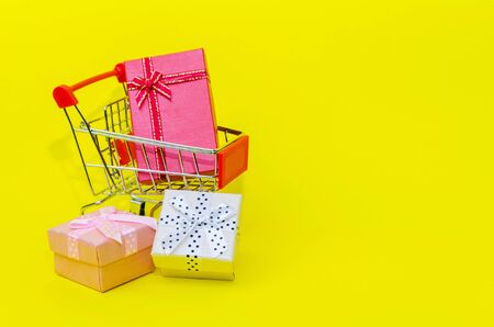 A mini supermarket shopping cart with mini colorful gift box on yellow background, holiday sale and shopping concept, selective focus, copy spaceの写真素材