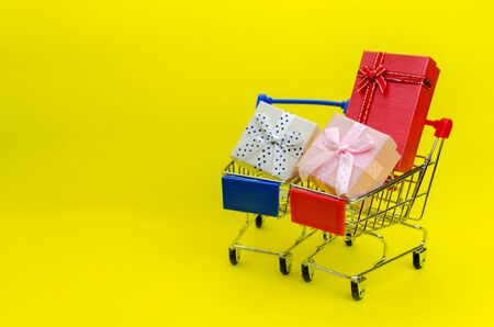 Two mini colorful gifts box in mini supermarket shopping cart on yellow backgroundの写真素材