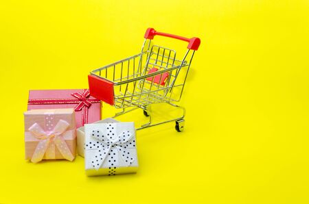 mini colorful gifts box in mini supermarket shopping cart on yellow background, holiday sale and online shopping concept, selective focus, copy spaceの写真素材