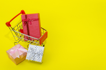 mini colorful gifts box in mini supermarket shopping cart on yellow background, holiday sale and online shopping concept, selective focus, copy spaceの写真素材