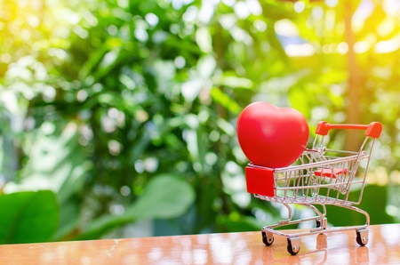 mini supermarket shopping cart with red heart for love on blurred green nature background , Valentine's Day concept, selective focus, copy space, sunlight effectの写真素材
