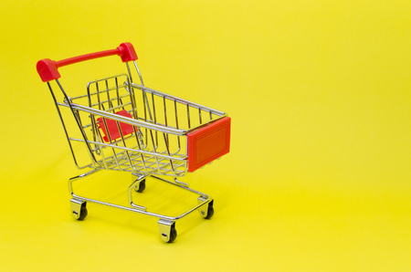 mini red color supermarket shopping cart on yellow background, holiday sale and online shopping concept, selective focus, copy spaceの写真素材